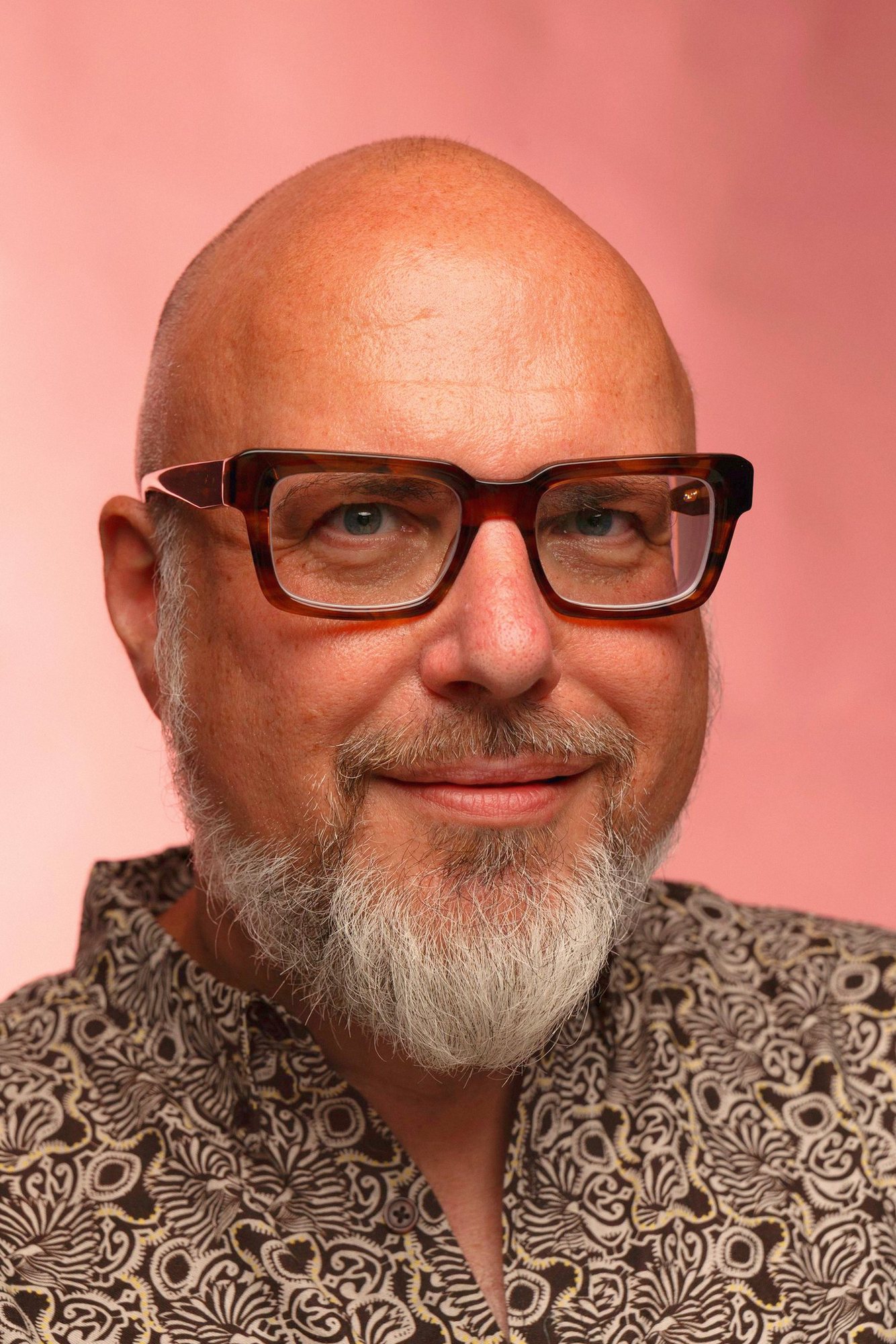 Sascha Schulz lächelt in die Kamera, dunkle Hornbrille, rosa Hintergrund